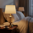 Lamp on a nightstand next to a bed with a cup and saucer