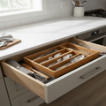 Open kitchen drawer with wooden utensil organizer containing forks, spoons, and knives.