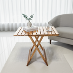 Wooden folding table with a plant, book, and glass of water in a living room setting.
