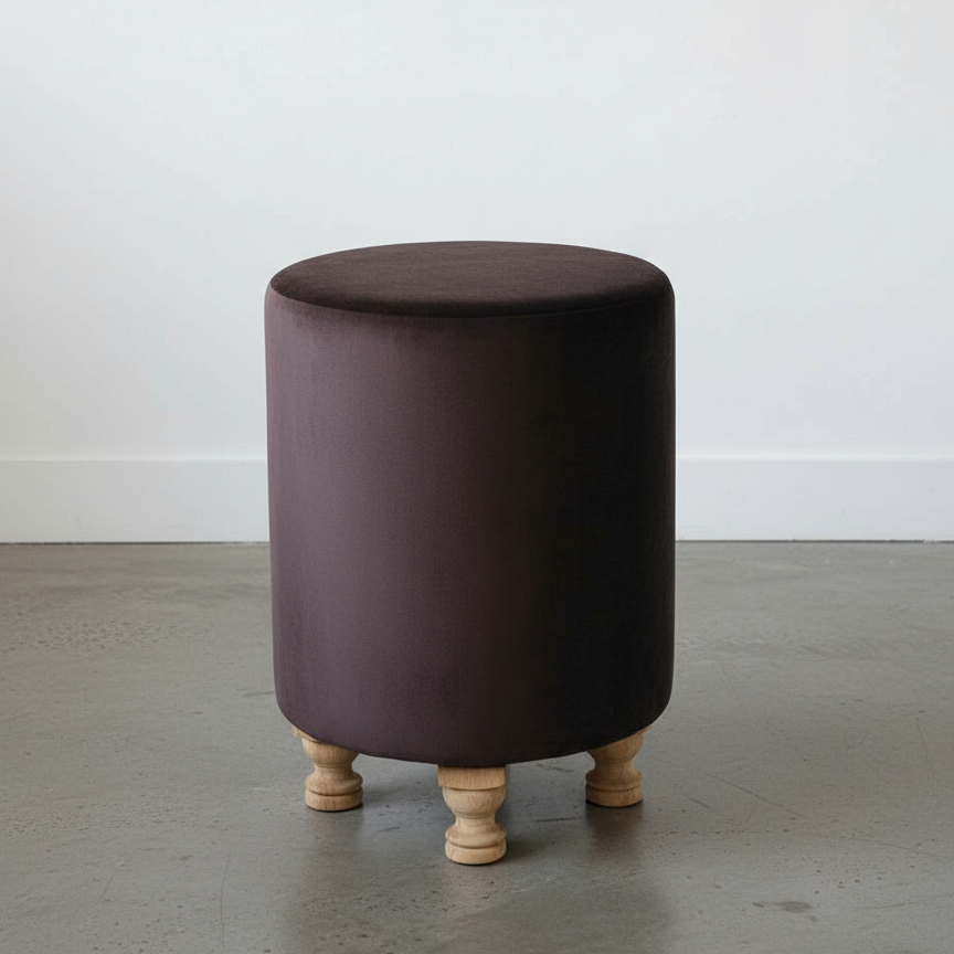 Round brown ottoman with wooden legs on a gray floor.