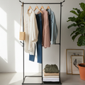 Clothing rack with clothes in a room with a plant and framed pictures.
