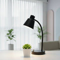 Black desk lamp on a surface with a potted plant in the background